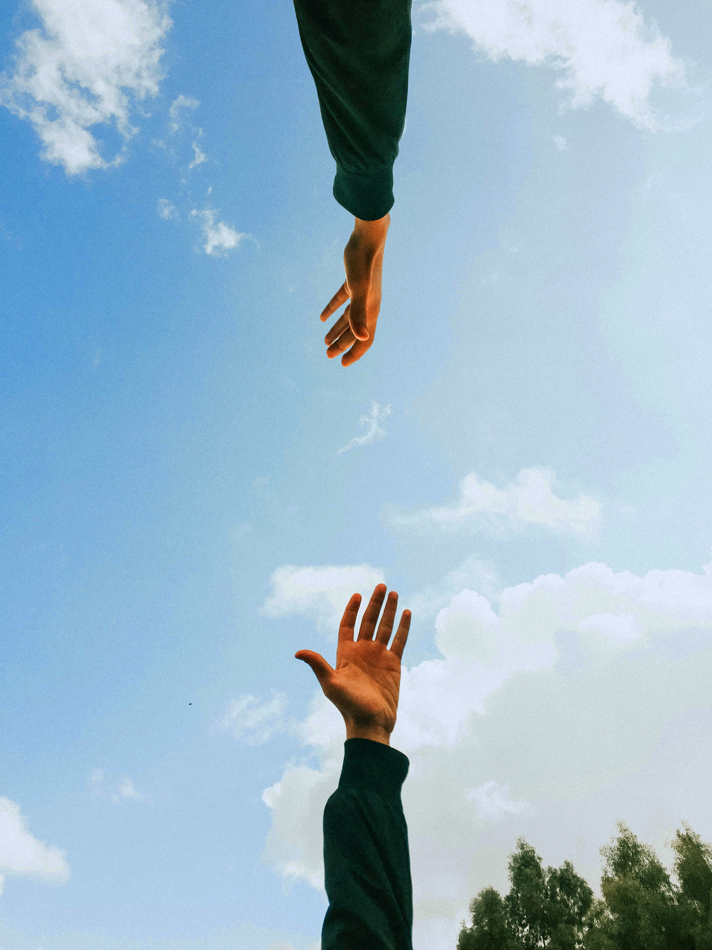 Two hands reaching towards each other against a blue sky